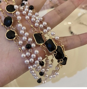 Detail of layered pearl necklace featuring black rectangular gemstones and gold plating