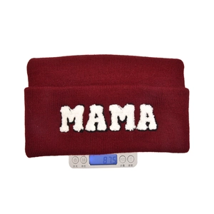 Burgundy knitted beanie with white MAMA embroidery on a scale showing 87.5g weight