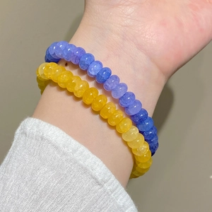 Gros plan de bracelets empilés en perles violettes et jaunes avec pendentif papillon au poignet