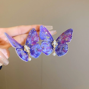 Detail of butterfly earring with purple gradient wings, gold foil, and pearl pendant