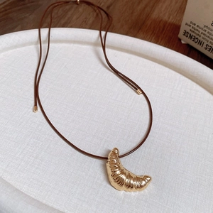 Detailed view of the gold croissant pendant with realistic texture on a brown leather cord