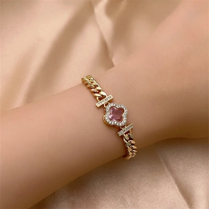 Detail of a gold clover bracelet with a pink gem and zircon on a silk background