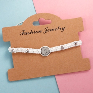 Close-up of white woven rope bracelet with Saint Benedict medal on a brown display card