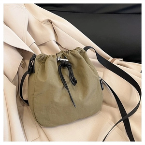 Detail of army green drawstring bucket bag with black strap on a beige trench coat