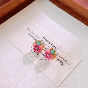 Macro shot of colorful floral stud earrings with pink and mint crystals on cream fabric