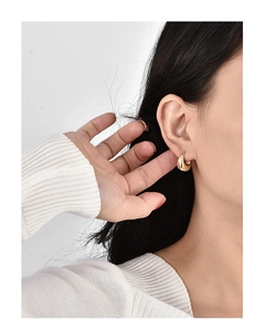 Close-up of polished gold-plated huggie hoop earring worn on an earlobe to show scale