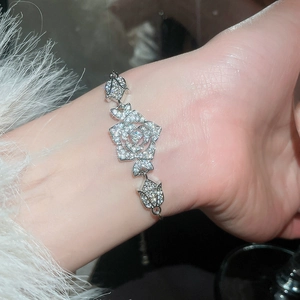 Macro detail of silver rose charm bracelet with white zircon pavé on female wrist