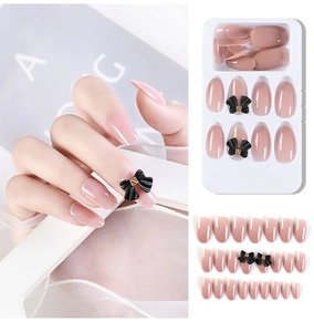 Detail of jelly pink press-on nails featuring 3D black bows and golden accents