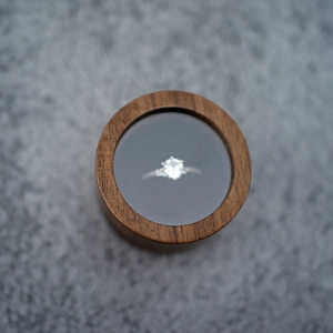Top view of a round black walnut wood ring box with a diamond ring on a grey surface