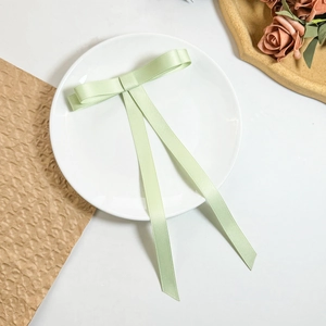 Detail of mint green satin bow hair clip with long ribbons on a ceramic plate