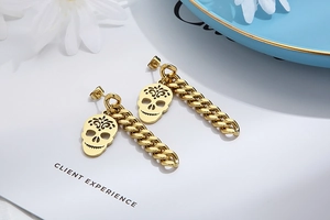 Detail shot of gold skull charm with thick curb chain earrings on a white floral card