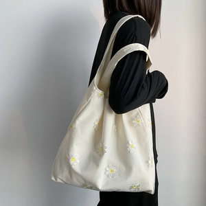 Detail of embroidered yellow daisies on an ivory canvas tote bag worn on shoulder