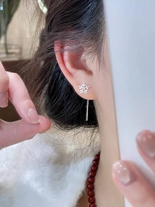 Detailed view of silver snowflake long chain earrings worn on a model's ear