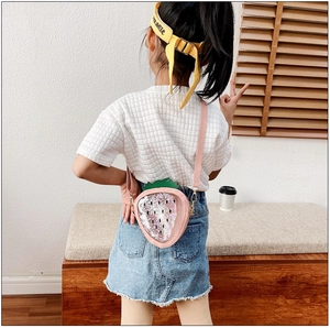 Pink strawberry-shaped crossbody bag with glitter sequins worn by a girl outdoors