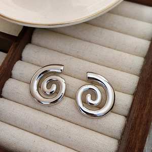Vue macro de boucles d'oreilles spirales en acier argenté sur plateau en velours beige