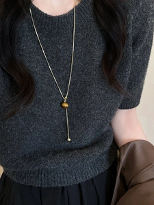 Detail of adjustable gold snake chain necklace with brown gemstone drop on grey sweater
