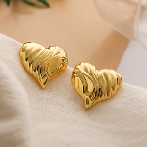Detail of gold heart earrings with textured surface on a white woven background