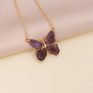 Detailed close-up of a golden necklace featuring a vibrant purple butterfly pendant