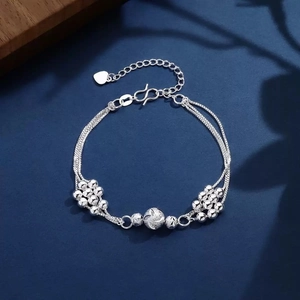 Macro shot of silver layered beaded chain bracelet with heart charm on blue surface