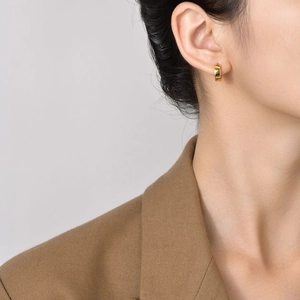 Close-up of minimalist polished gold hoop earrings worn by a model in a brown blazer