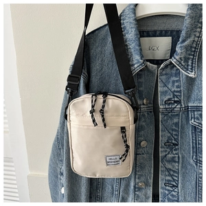 Detail view of beige nylon crossbody bag hanging on a denim jacket for outdoor style