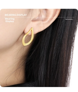 Detailed close-up of a gold water-drop shaped earring with brushed metal texture