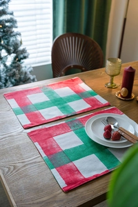 Detail of red and green plaid Christmas placemats on wooden table with holiday decor