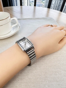 Detail of a square silver quartz watch with a metal link strap on a woman wrist
