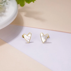 Detailed view of heart-shaped white shell earrings with gold plating on a geometric background