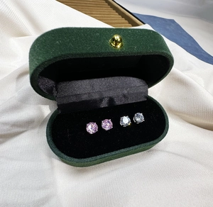 Macro detail of classic pink and white round-cut zircon studs in a green velvet jewelry box