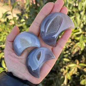 Three moon-shaped agate geodes with blue crystals held by hand in natural light