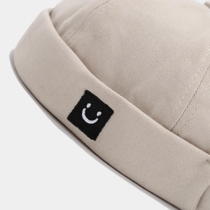 Beige cotton docker hat featuring a square smiley face embroidery in a 45-degree side view