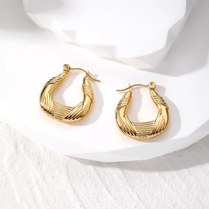 Detail of gold twisted hoop earrings with textured vertical stripes and metallic finish