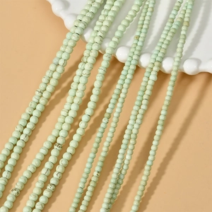 Strands of 3-4mm light green turquoise beads with natural texture on a white ceramic dish