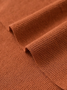 Macro shot of knit fabric texture in terracotta hue showing ribbed pattern and soft draping