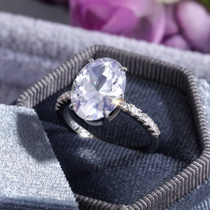Makroaufnahme eines silbernen Rings mit ovalem Zirkon in Samtschachtel vor Blumen