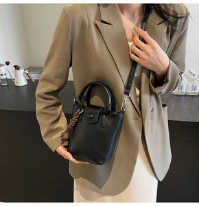 Detail of a chic black leather bucket bag with metal ring handle and woven charm