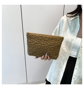 Detail of flower quilted texture and pleats on a brown clutch handbag held by a model