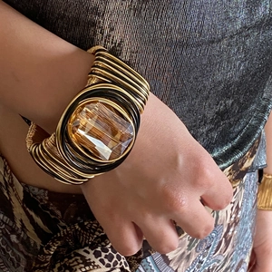 Detail of a braided gold and black wire cuff bracelet with a large amber crystal gemstone
