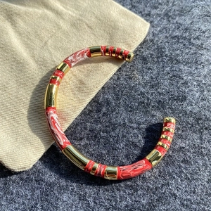 Detail view of a gold-tone open C-cuff bracelet with alternating red and white enamel motifs