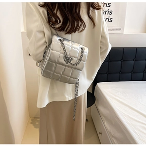 Detail of silver quilted backpack with heart-shaped metal buckle and chain straps