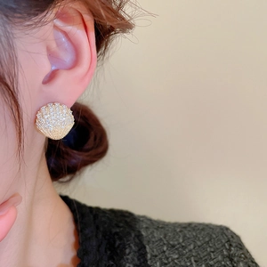 Macro detail of gold fan earrings with zircons and shell texture on female ear