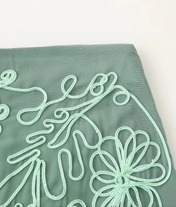 Detail of sage green fabric with floral cord embroidery and textured crepe material