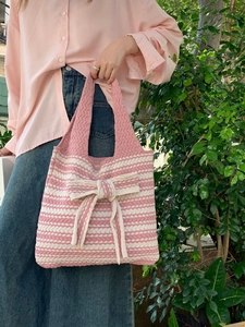 Detail of pink and white striped knit tote bag with a large bow decoration and soft texture