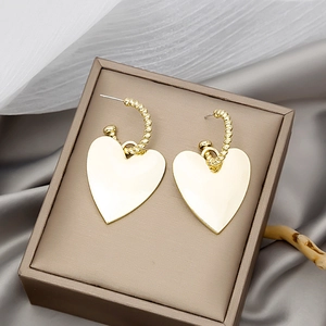 Detailed view of large gold heart drop earrings resting on silk fabric in a jewelry box