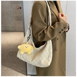 Close-up of beige woven plaid hobo bag with a yellow star plush charm on a model