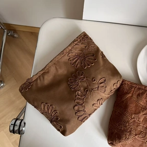 Detailed view of camel suede cosmetic bag with 3D floral embroidery on a white table