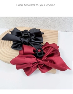 Macro detail of large black and burgundy satin bow hair claws on a wooden tray
