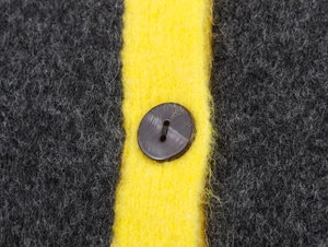Detail of grey fuzzy knit fabric with yellow contrast stripe and brown button