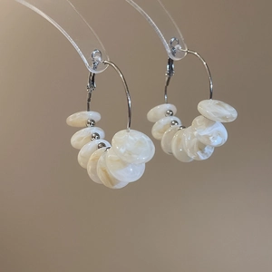 Detail of silver hoop earrings featuring cream resin flat beads on professional stand